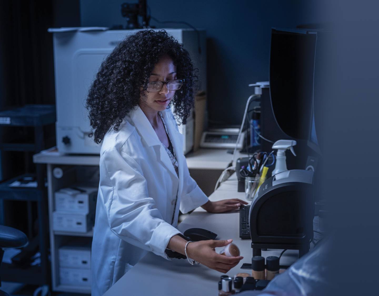 A woman working in a lab looking at a small bottle